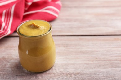 Photo of Tasty mustard sauce in jar on wooden table, space for text