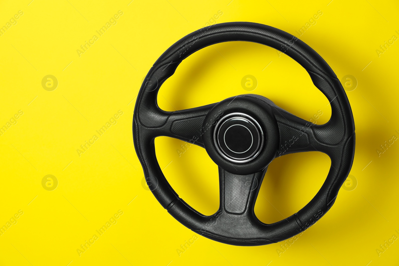 Photo of New black steering wheel on yellow background, space for text