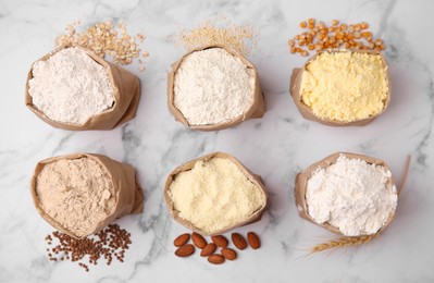 Photo of Paper bags with different types of flour and ingredients on white marble table, flat lay