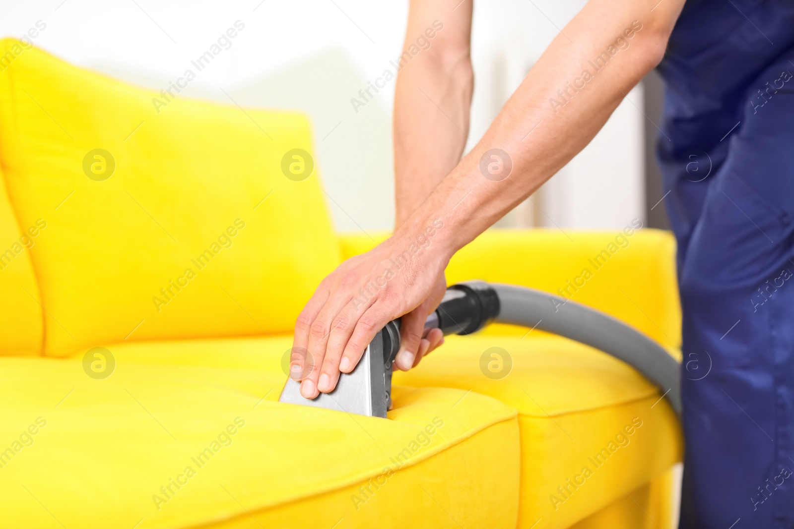 Photo of Dry cleaning worker removing dirt from sofa indoors