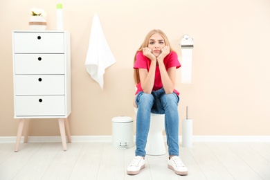 Photo of Young woman sitting on toilet bowl at home