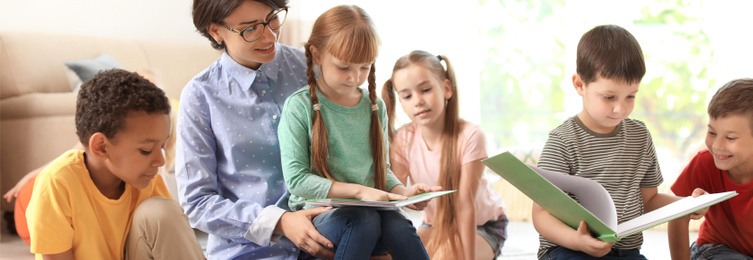 Image of Young nanny reading book and little children indoors. Banner design 