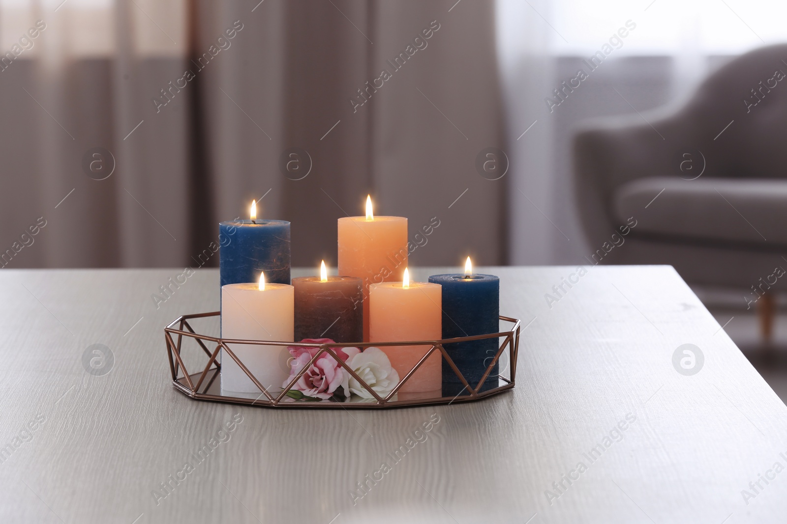 Photo of Tray with burning candles and flowers on table in living room