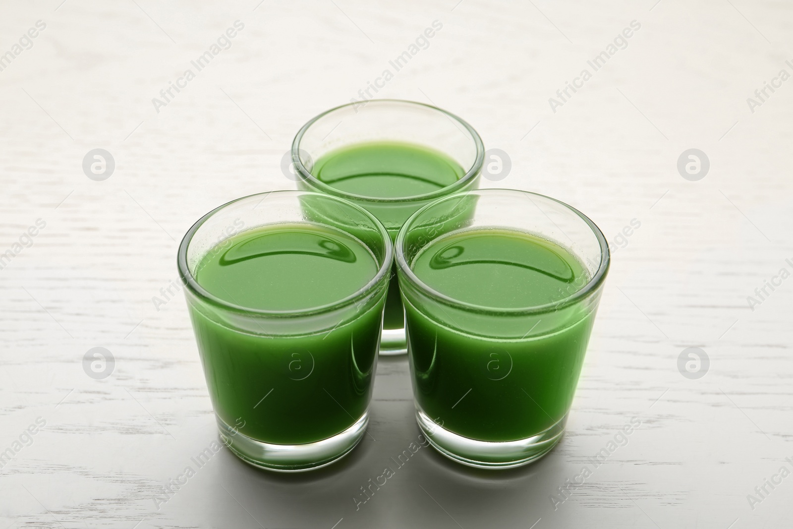 Fresh wheat grass juice in glasses on white wooden background Photo of Fresh wheat grass juice in glasses on white wooden background