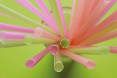 Different plastic straws on green background, above view