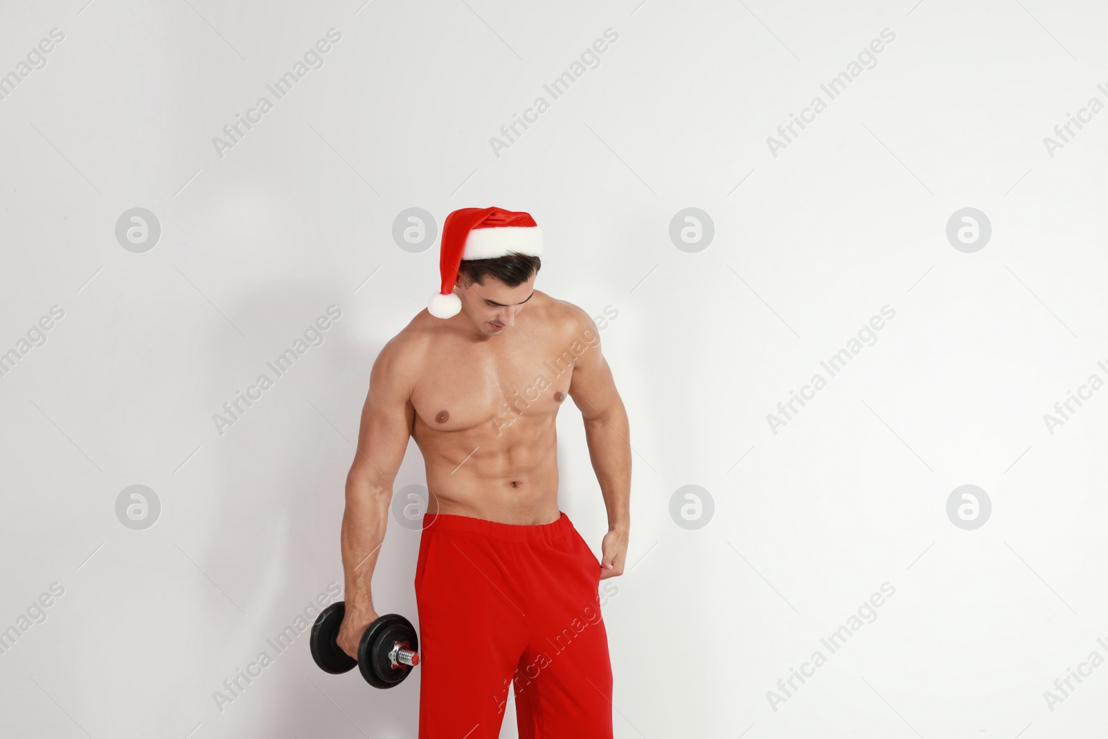Photo of Sexy shirtless Santa Claus with dumbbell on light background