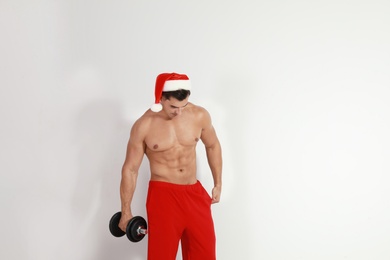 Sexy shirtless Santa Claus with dumbbell on light background