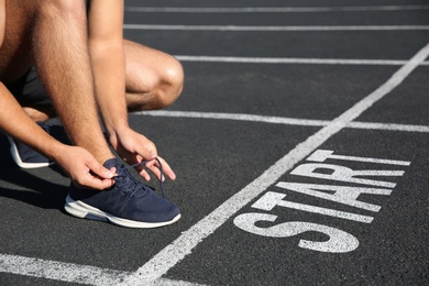 Image of Sporty man tying shoelaces in front of starting line at stadium, closeup