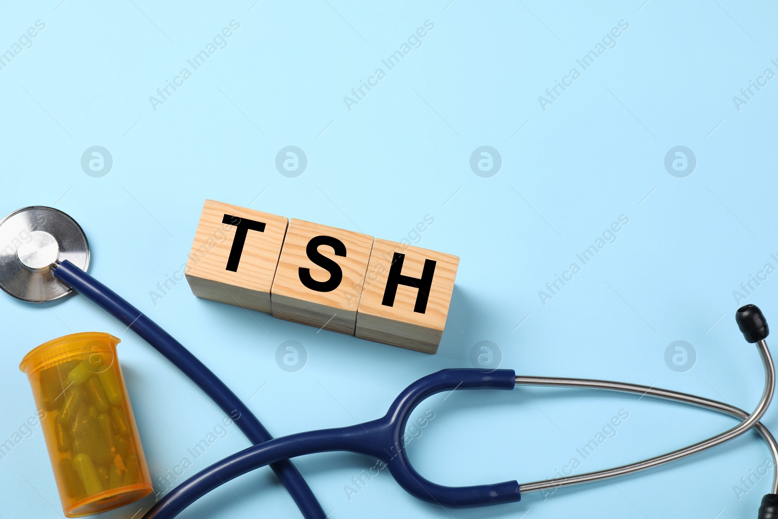 Photo of Endocrinology. Stethoscope, pills and wooden cubes with thyroid hormones on light blue background. Space for text