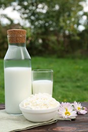 Photo of Tasty fresh milk and cottage cheese on wooden table outdoors