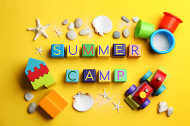 Colorful wooden cubes with phrase SUMMER CAMP on yellow background, flat lay