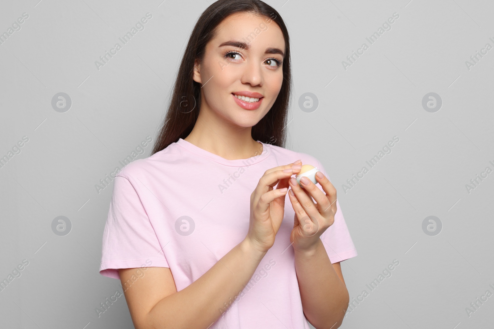 Photo of Young woman with lip balm on grey background