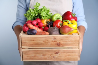 Photo of Farmer with wooden crate full of different vegetables and fruits on blue background, closeup. Harvesting time