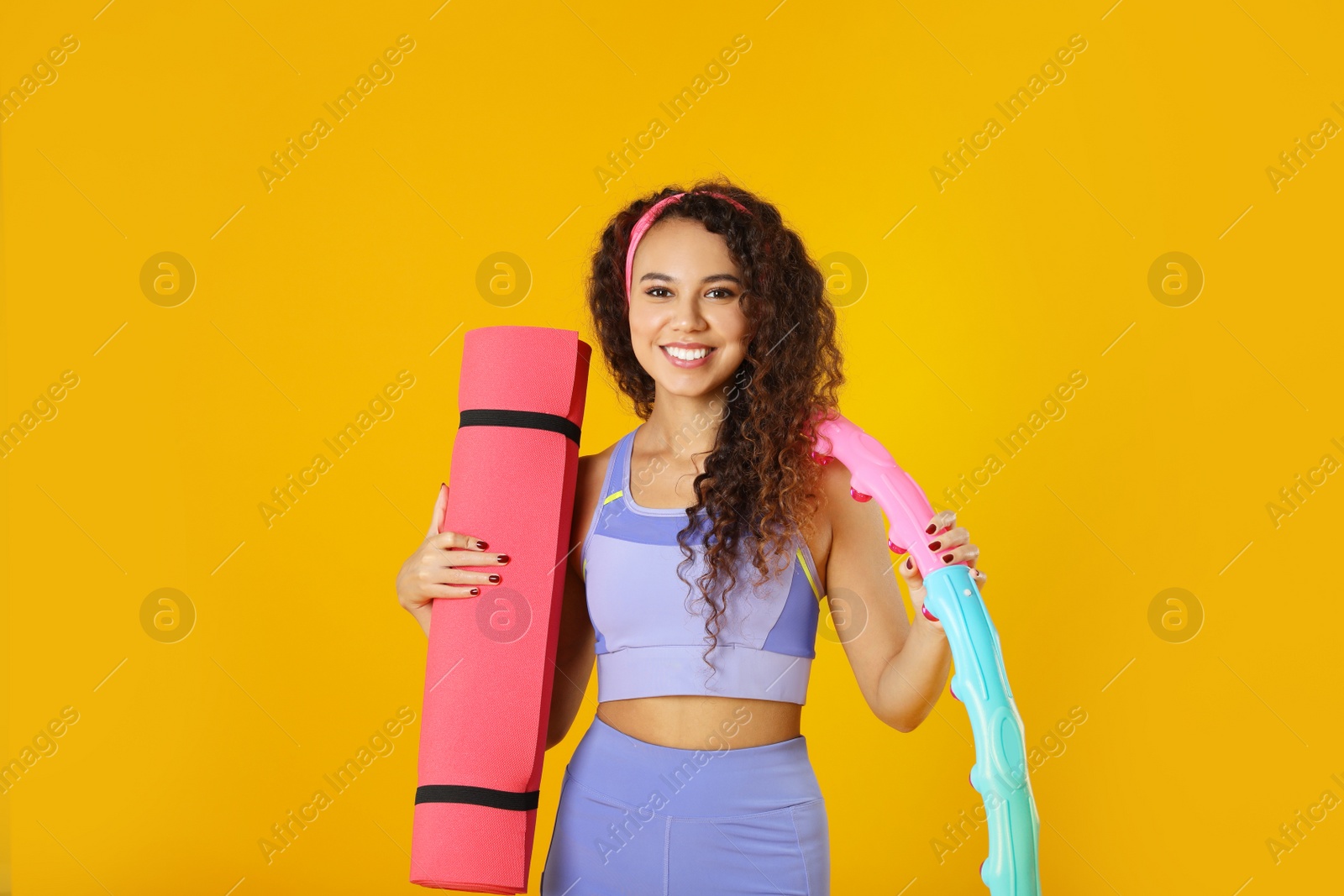 Photo of Beautiful African American woman with yoga mat and hula hoop on yellow background