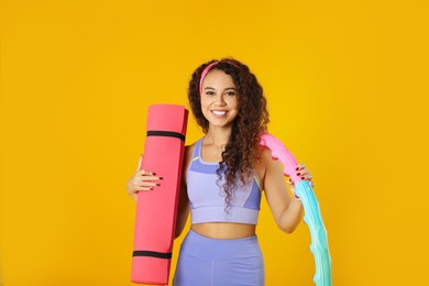 Photo of Beautiful African American woman with yoga mat and hula hoop on yellow background
