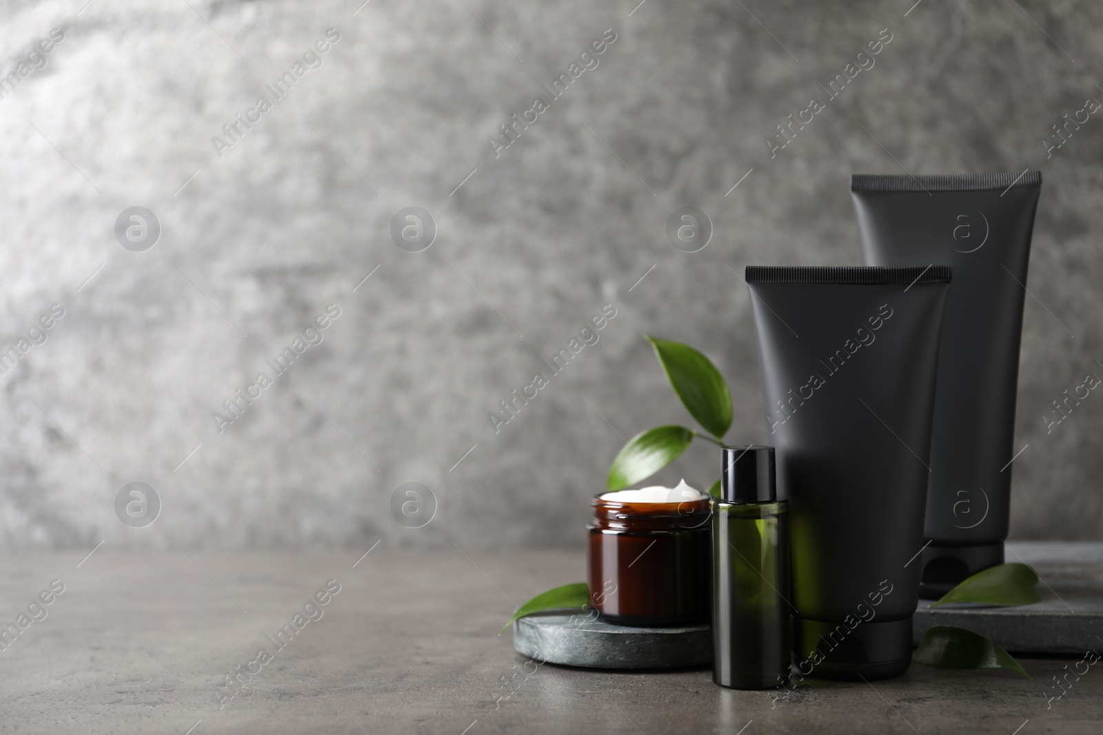 Photo of Facial cream and other men's cosmetic with green leaves on grey stone table. Mockup for design