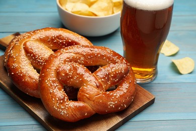 Tasty freshly baked pretzels and glass of beer on light blue wooden table, closeup