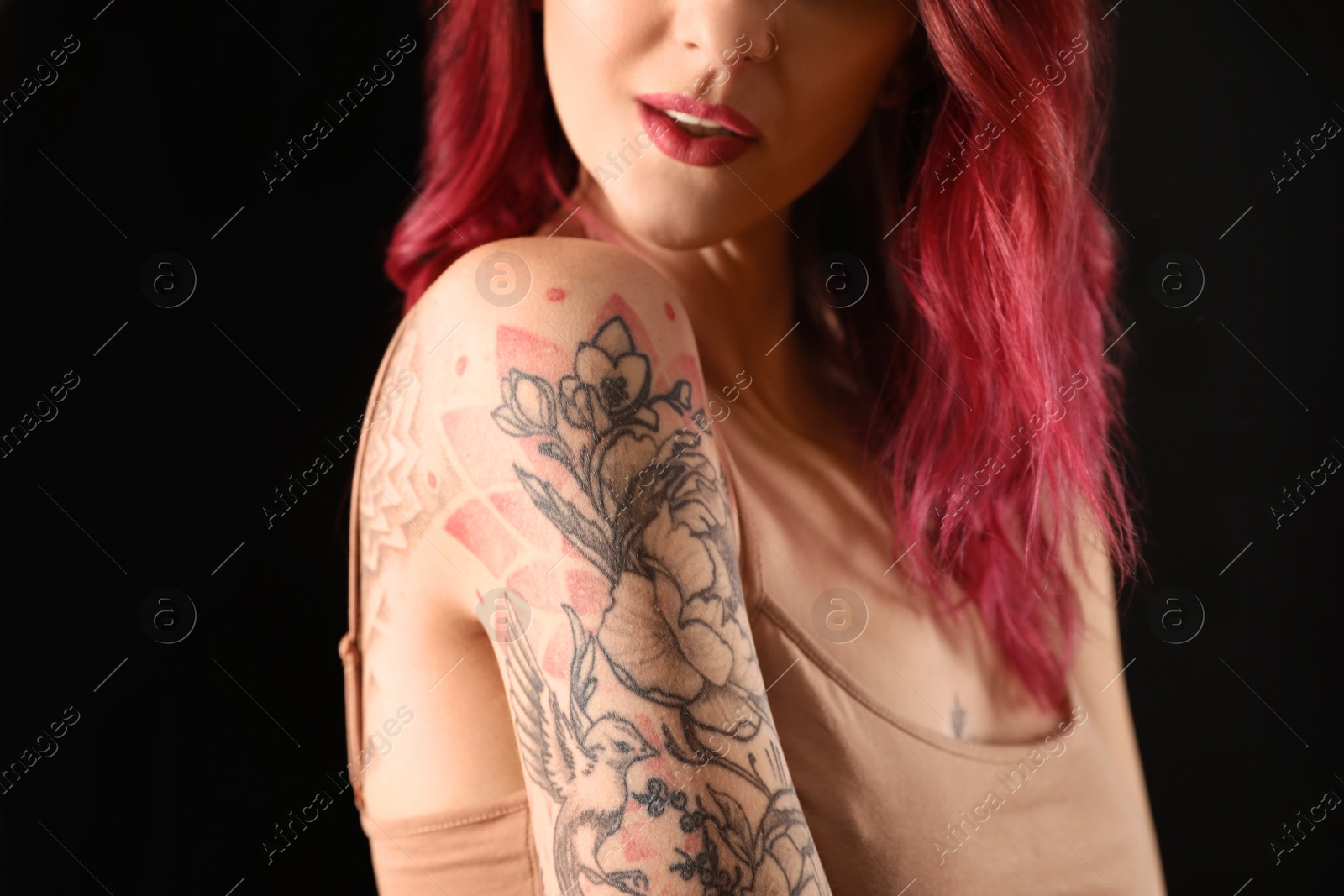 Photo of Beautiful woman with tattoos on body against black background, closeup