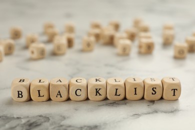 Photo of Wooden cubes with word Blacklist on white marble table, closeup