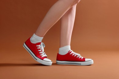 Woman wearing red classic old school sneakers on brown background, closeup