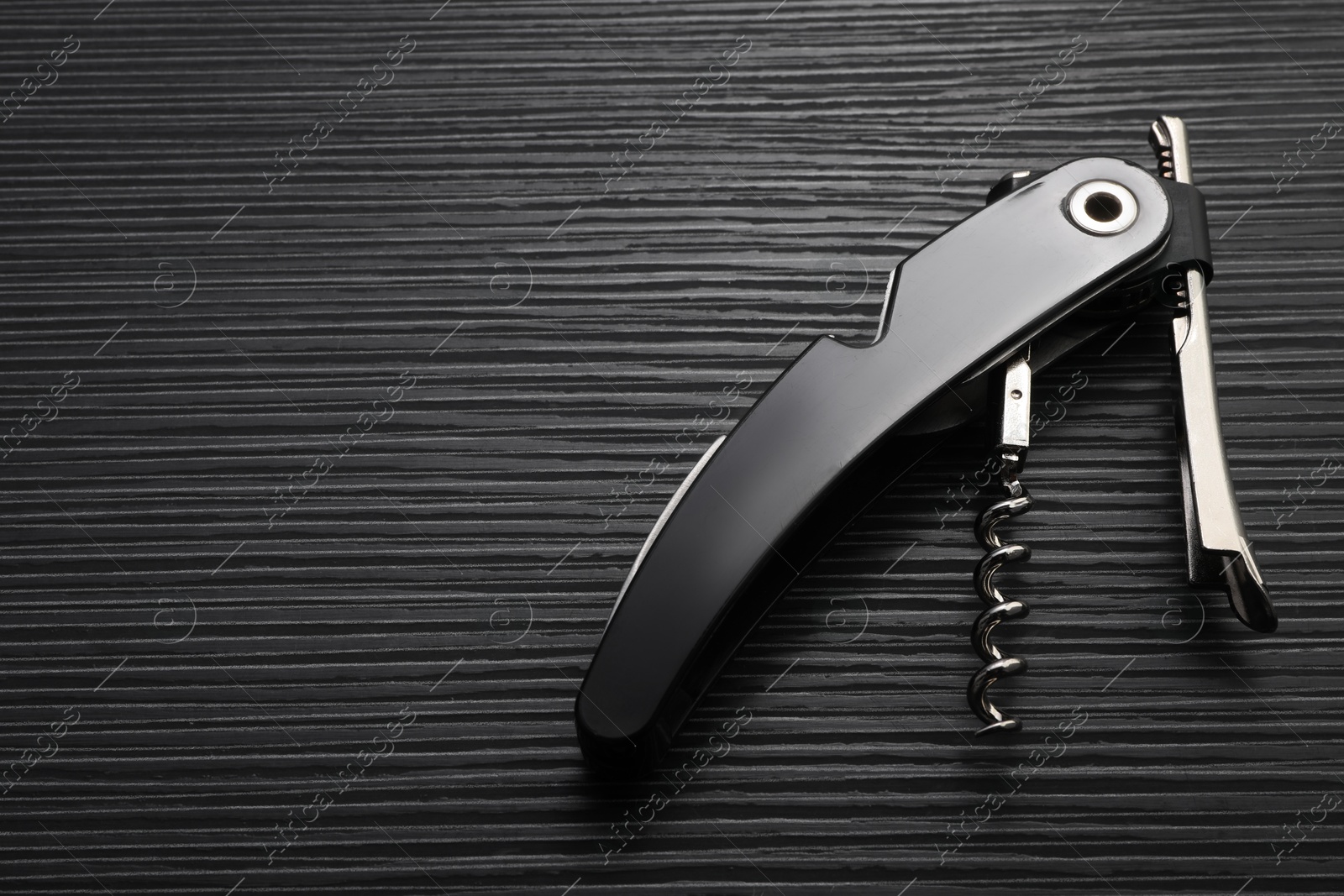 Photo of One corkscrew (sommelier knife) on black wooden table, top view. Space for text