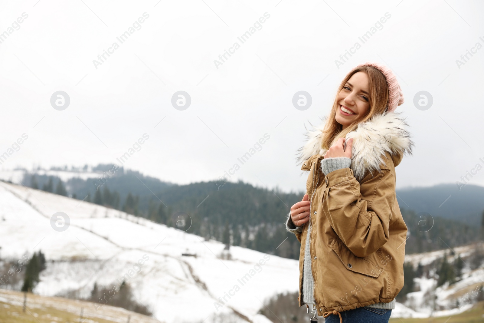 Photo of Young woman in warm clothes near snowy hill, space for text. Winter vacation