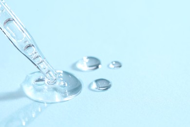 Glass pipette and transparent liquid on light blue background, closeup. Space for text