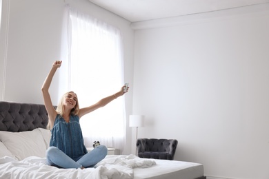 Photo of Young woman operating air conditioner with remote control at home