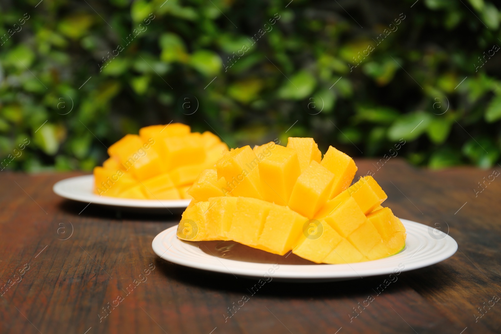 Photo of Delicious ripe cut mangos on wooden table outdoors