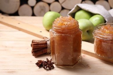 Delicious apple jam in jars, fresh fruits and spices on wooden table