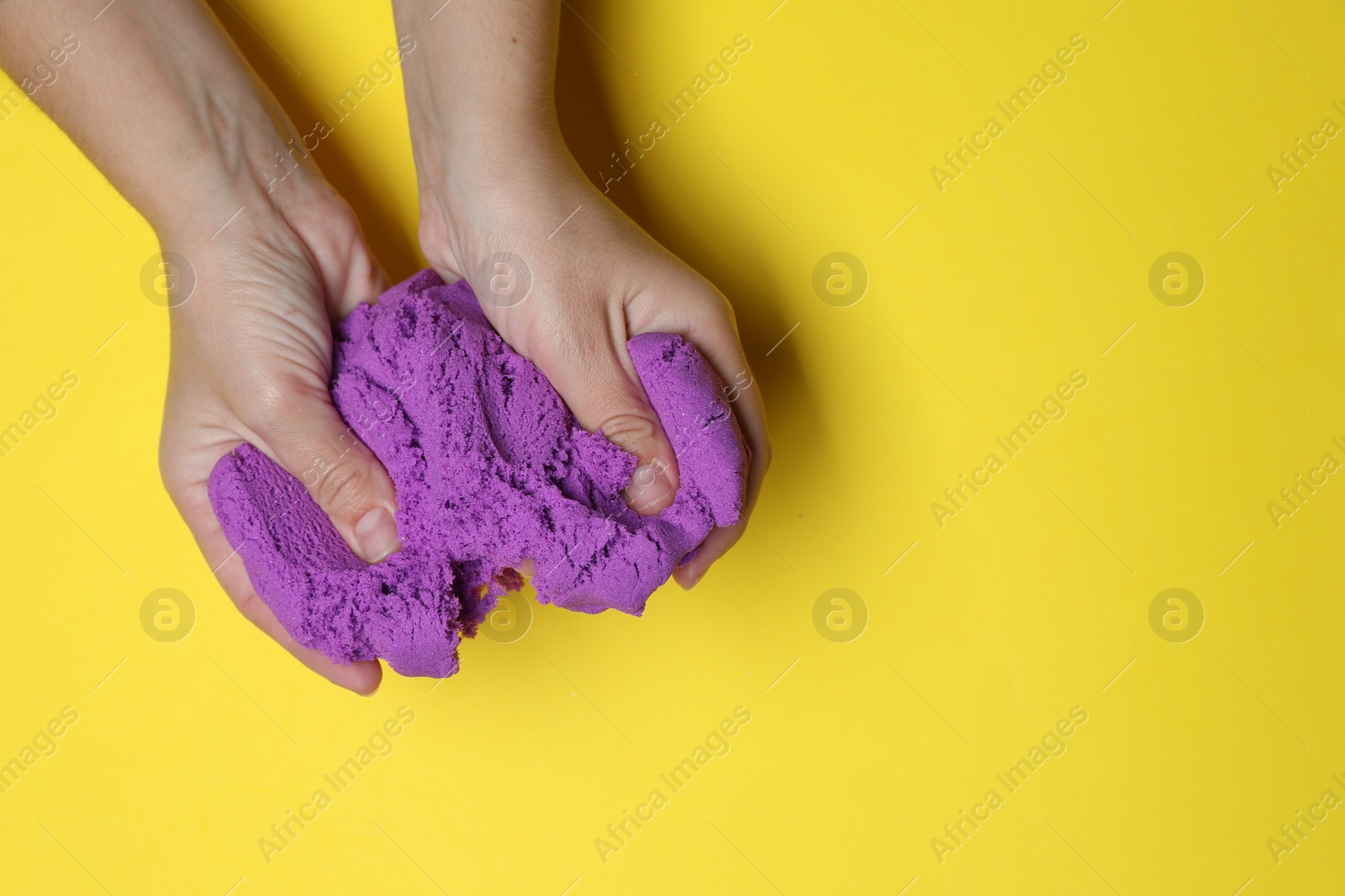 Photo of Woman playing with kinetic sand on yellow background, top view. Space for text