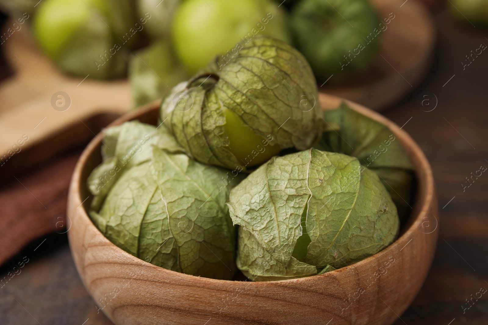 Photo of Fresh green tomatillos with husk in bowl on table, closeup