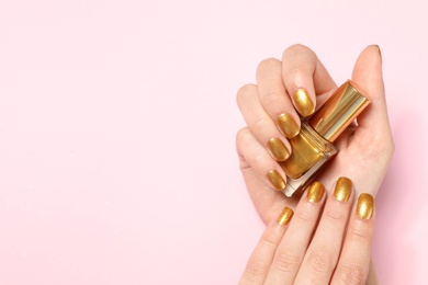 Woman holding bottle of golden nail polish in manicured hand on color background, top view. Space for text