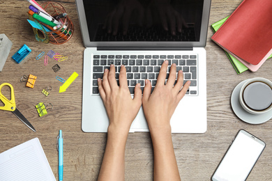 Female designer working with laptop at wooden table, top view