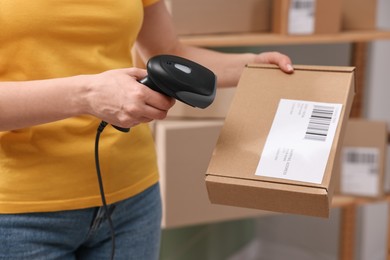 Photo of Parcel packing. Post office worker with scanner reading barcode indoors, closeup