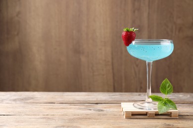 Photo of Refreshing light blue cocktail on wooden table, space for text