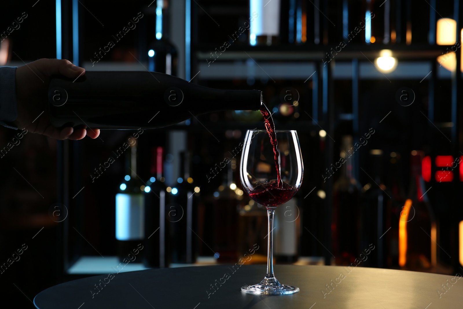 Photo of Man pouring red wine from bottle into glass indoors, closeup