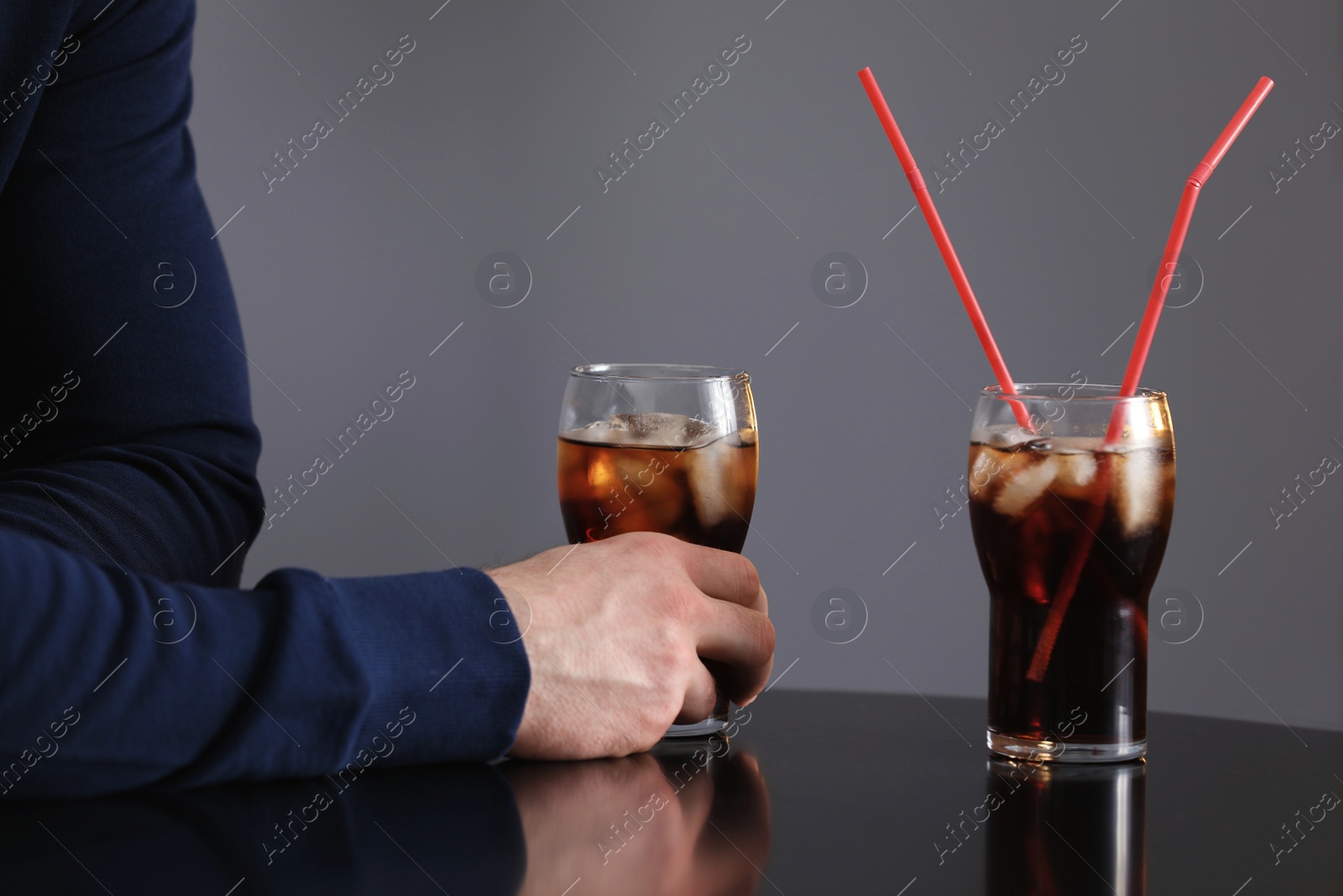 Photo of Man with glass of iced cola at table against grey background, closeup