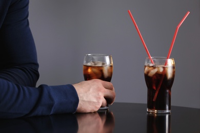 Man with glass of iced cola at table against grey background, closeup