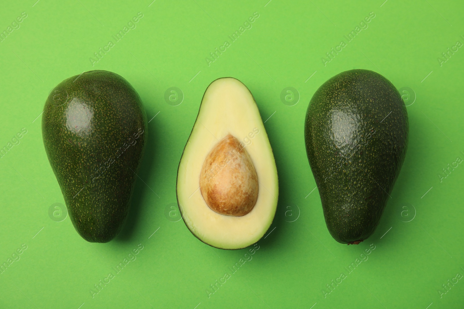 Photo of Cut and whole fresh ripe avocados on green background, flat lay