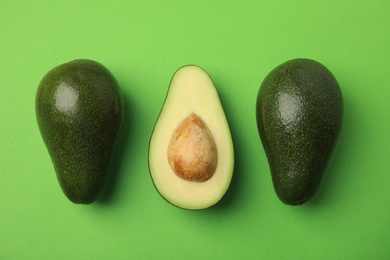 Cut and whole fresh ripe avocados on green background, flat lay