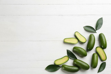 Fresh seedless avocados with green leaves on white wooden table, flat lay. Space for text