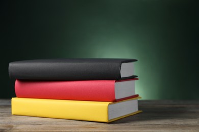 Learning foreign language. Flag of Germany made of books on wooden table against dark green background, space for text