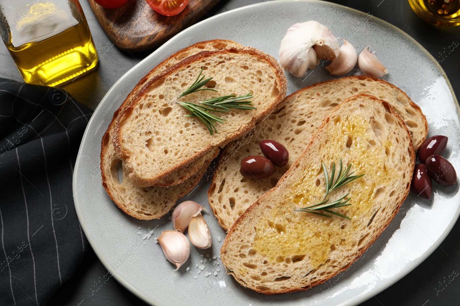 Photo of Tasty bruschettas with oil and rosemary on black table, flat lay