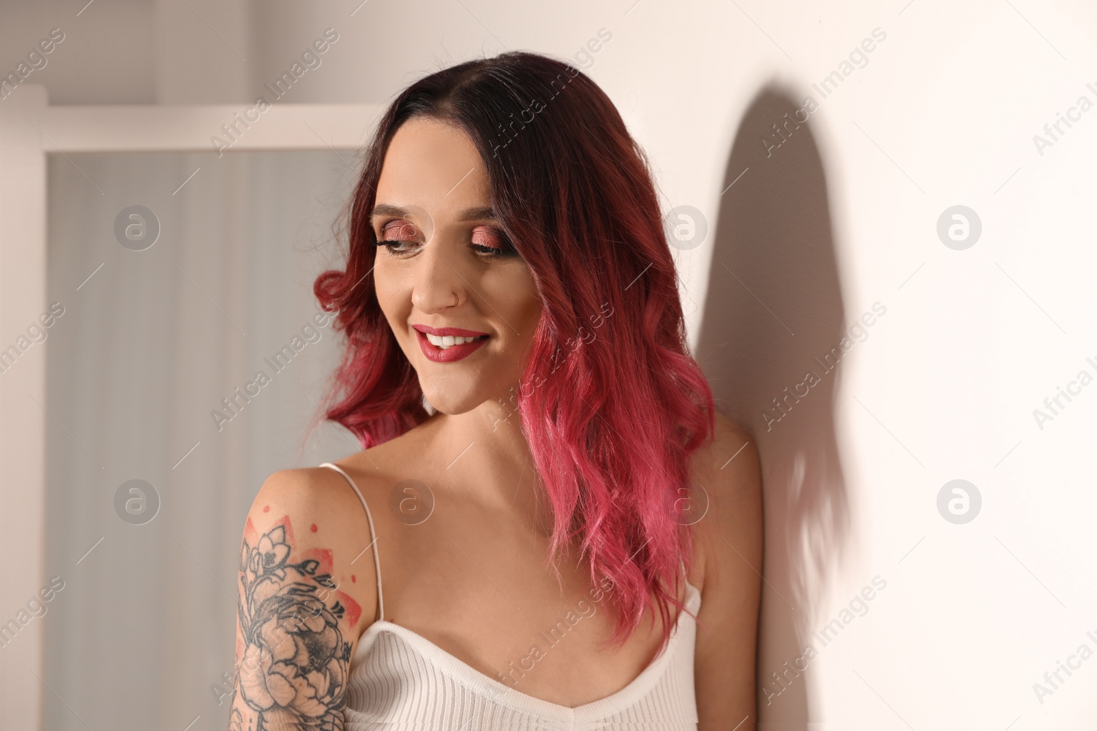 Photo of Beautiful woman with tattoos on arm near mirror indoors