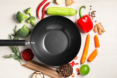 Empty iron wok surrounded by raw ingredients on white wooden table, flat lay