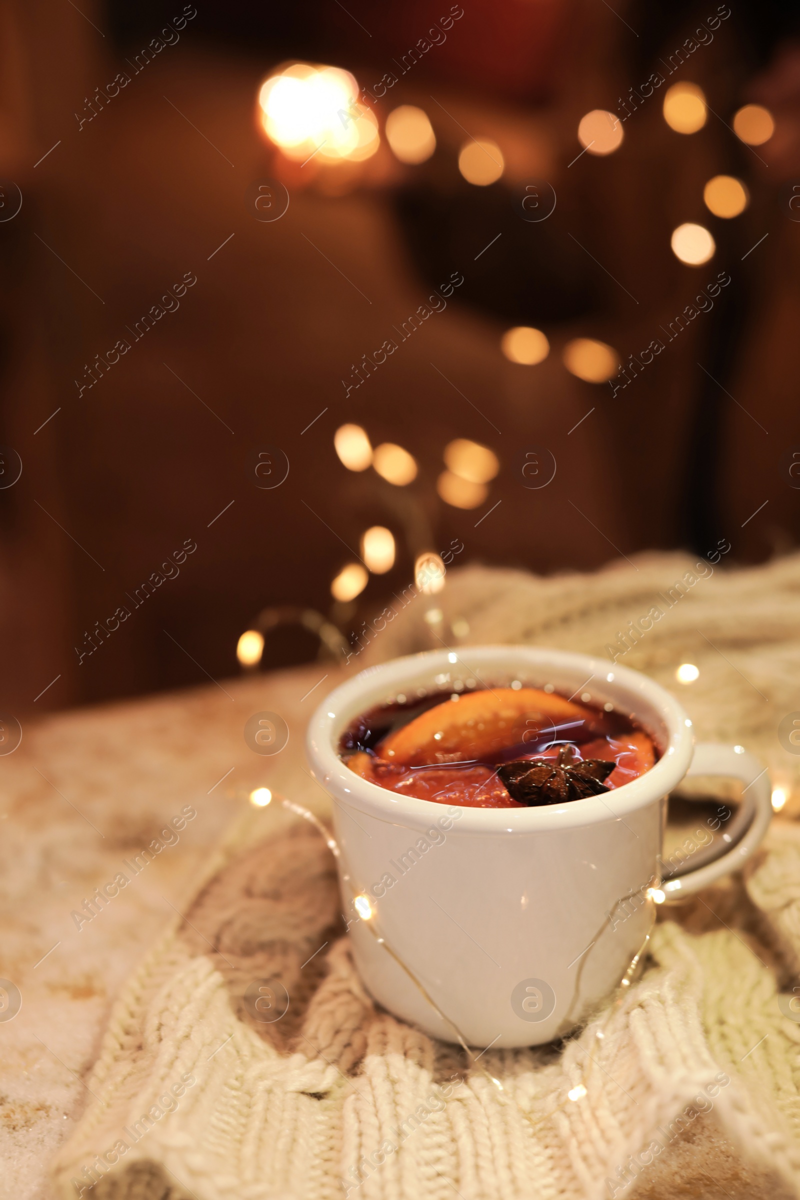 Photo of Cup of hot mulled wine and garland on table against blurred background. Space for text