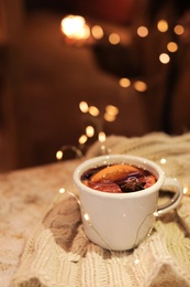 Photo of Cup of hot mulled wine and garland on table against blurred background. Space for text