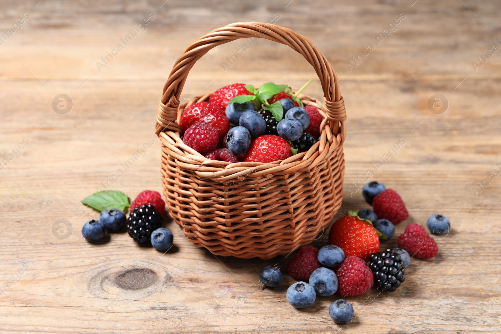 Photo of Wicker basket with many different fresh ripe berries on wooden table