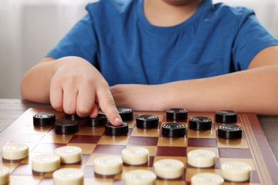 Photo of Playing checkers. Boy thinking about next move at table in room, closeup